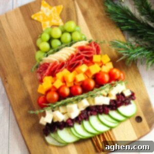 Charcuterie board shaped like a Christmas tree with cheese, cucumbers, tomatoes, grapes, salami, etc...