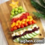 Charcuterie board shaped like a Christmas tree with cheese, cucumbers, tomatoes, grapes, salami, etc...