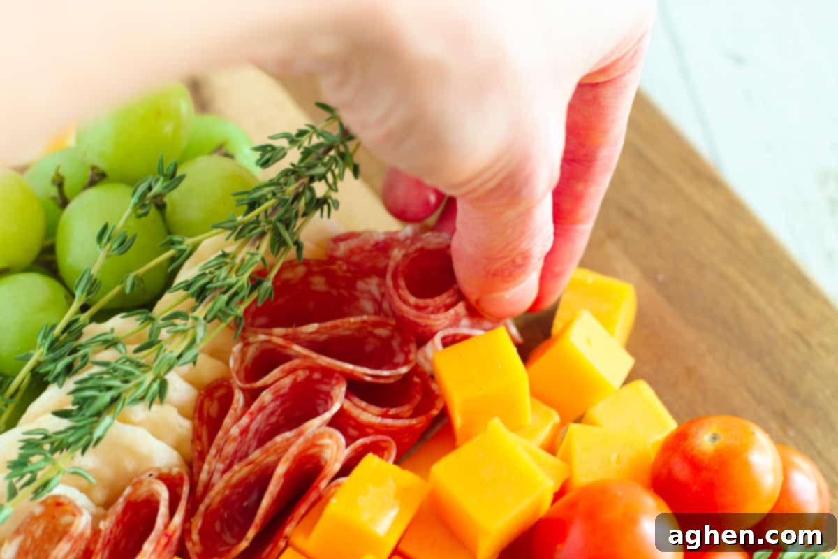 A hand expertly placing folded slices of salami onto the charcuterie board, forming a textured layer of the Christmas tree.