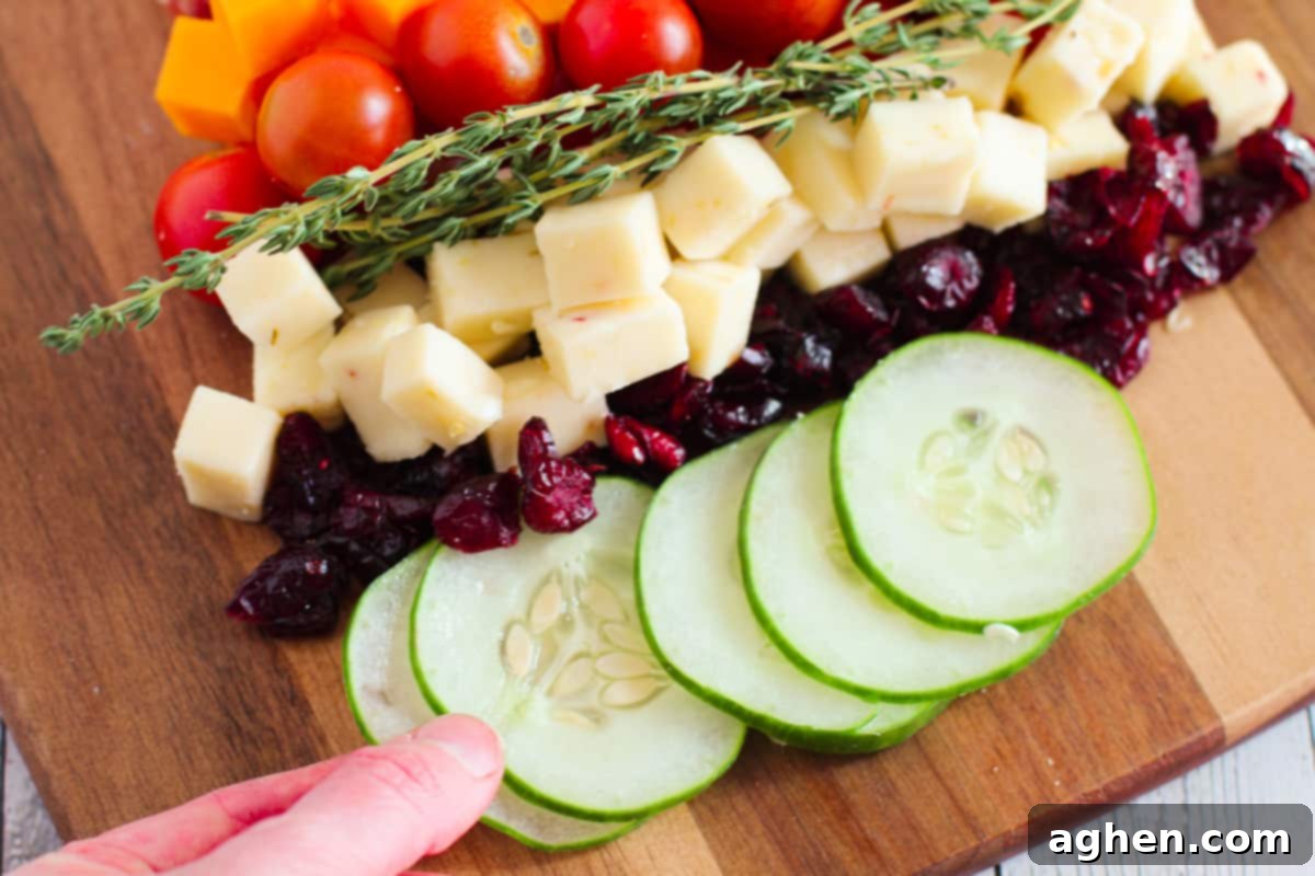 A hand gently placing fresh cucumber slices onto the charcuterie board, adding a vibrant green layer to the Christmas tree design.