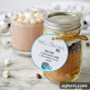 Homemade hot cocoa mix in a mason jar with a gift tag and a mug of hot chocolate with marshmallows behind it.