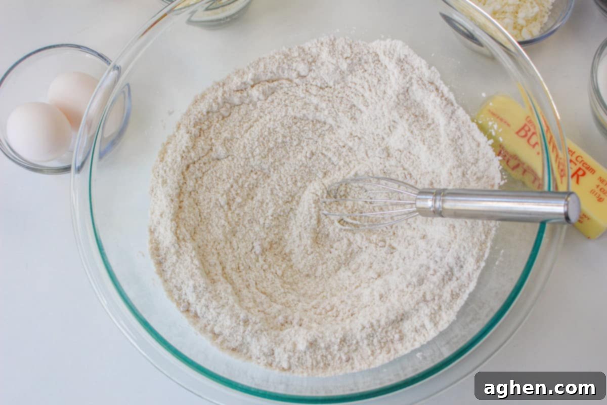 A glass bowl containing dry cake ingredients (flour, sugars, baking soda, salt) with a whisk ready to combine them.