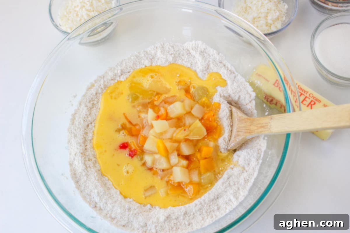 Wet ingredients, including fruit cocktail with syrup, eggs, and vanilla, being added to the bowl of dry ingredients for the cake batter.