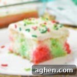 Christmas poke cake with pockets of red and green color throughout a fluffy white sheet cake and vanilla frosting with red and green sprinkles.