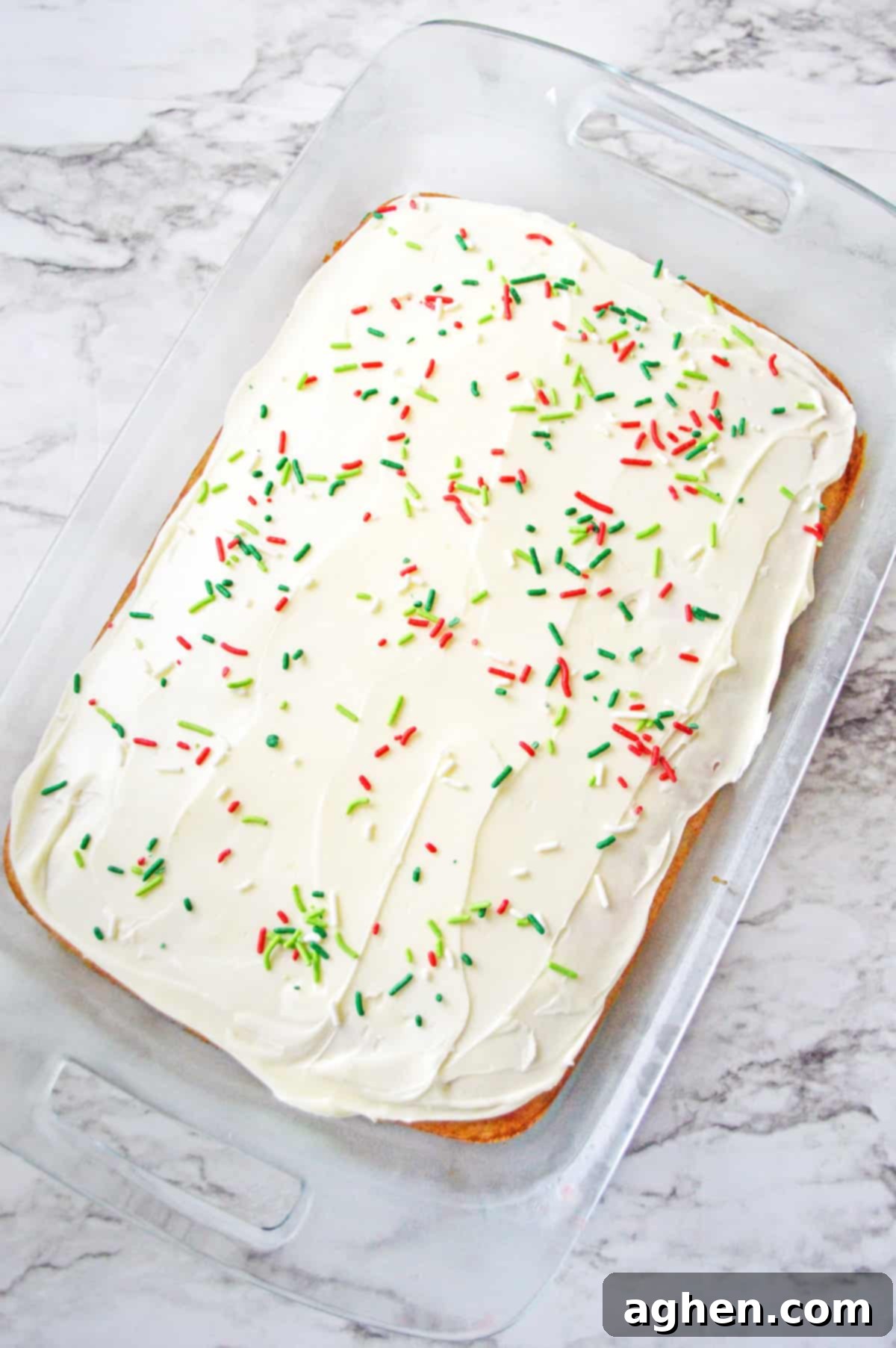 Rectangular cake in 9x13 baking dish topped with vanilla frosting and christmas sprinkles, showcasing the final decorated poke cake.
