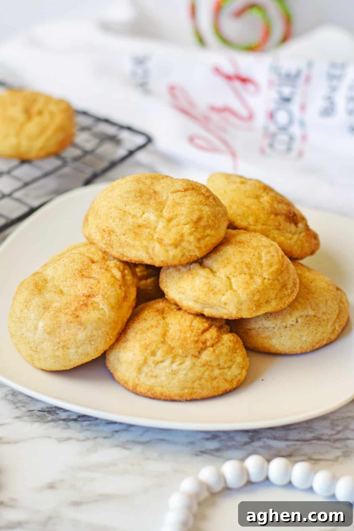 Snickerdoodle cake mix cookies stacked in a pile on a white plate with a cooling rack with more snickerdoodles behind them.