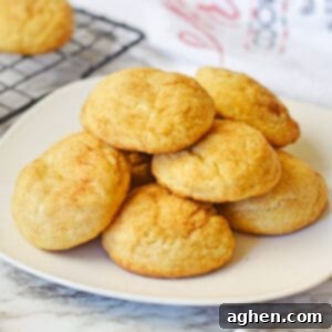 Snickerdoodle cake mix cookies stacked in a pile on a white plate with a cooling rack with additional snickerdoodles behind them.