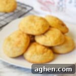 Snickerdoodle cake mix cookies stacked in a pile on a white plate with a cooling rack with additional snickerdoodles behind them.