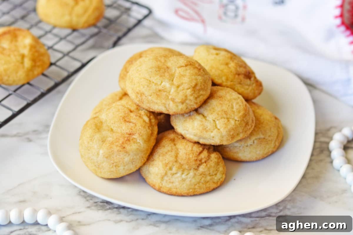 Thick snickerdoodle cake mix cookies piled on a white plate with more cookins on a cooling rack in the background.