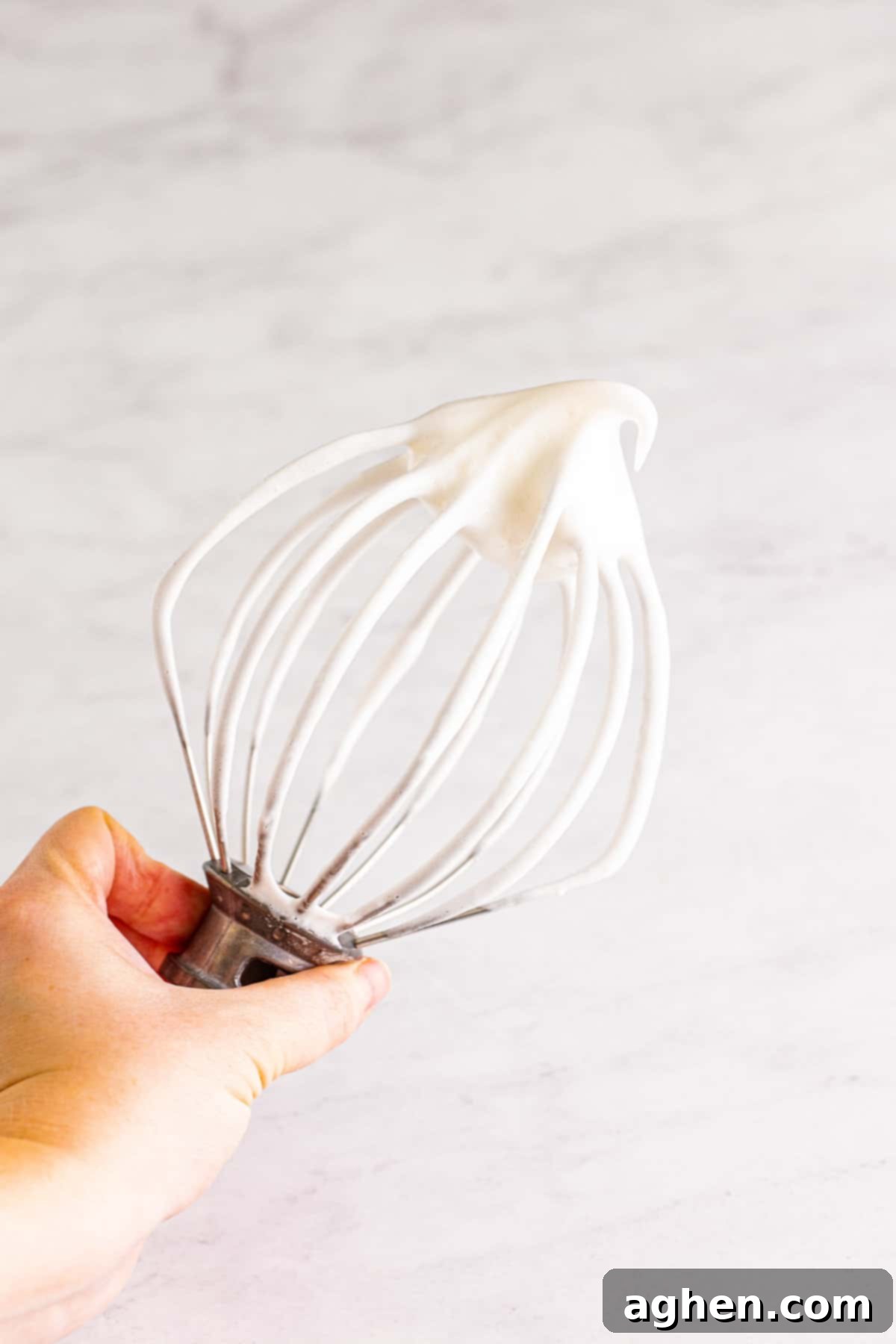 Egg whites forming soft peaks on wire whisk mixer attachment.
