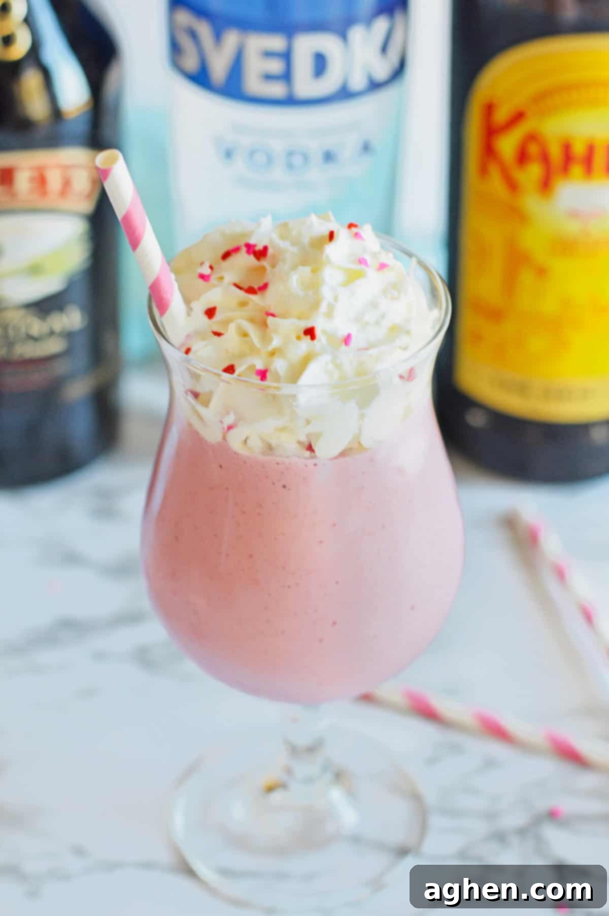 Pink strawberry mudslide in a glass with Kahlua, vodka, and Baileys bottles behind it.