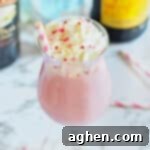 Pink strawberry mudslide in a glass with Kahlua and Baileys bottles behind it.
