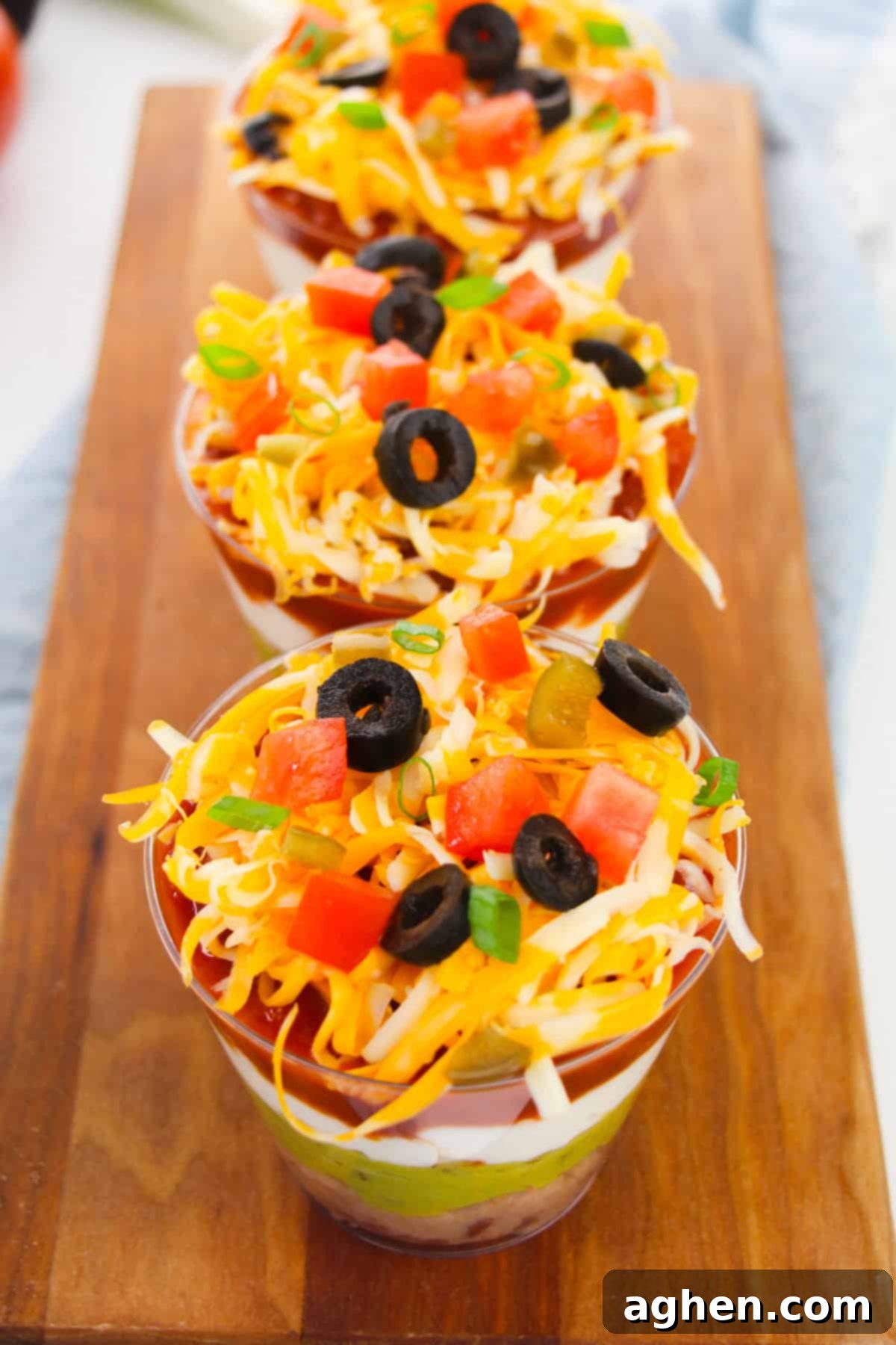 Individual taco dip cups lined up on a rustic serving board, ready for guests to enjoy. Each cup is filled with colorful layers and topped with fresh ingredients.
