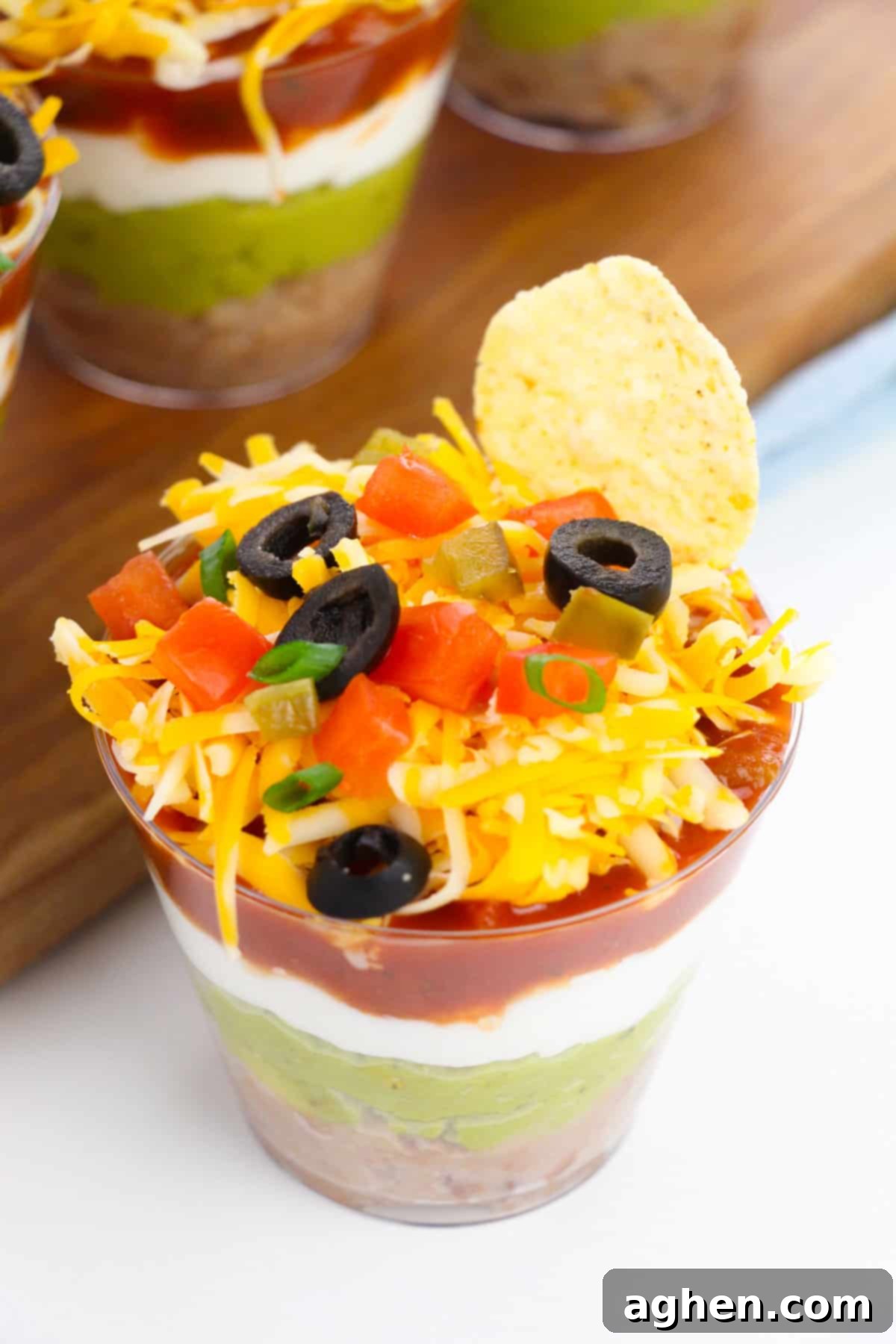 A single 7 layer taco dip cup featuring a tortilla chip sticking out, ready to be enjoyed as a perfect party appetizer.