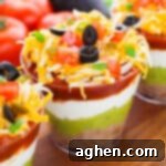 7 layer dip cups with refried beans, guacamole, sour cream, salsa, cheese, olives, green onions, tomatoes, and jalapenos.