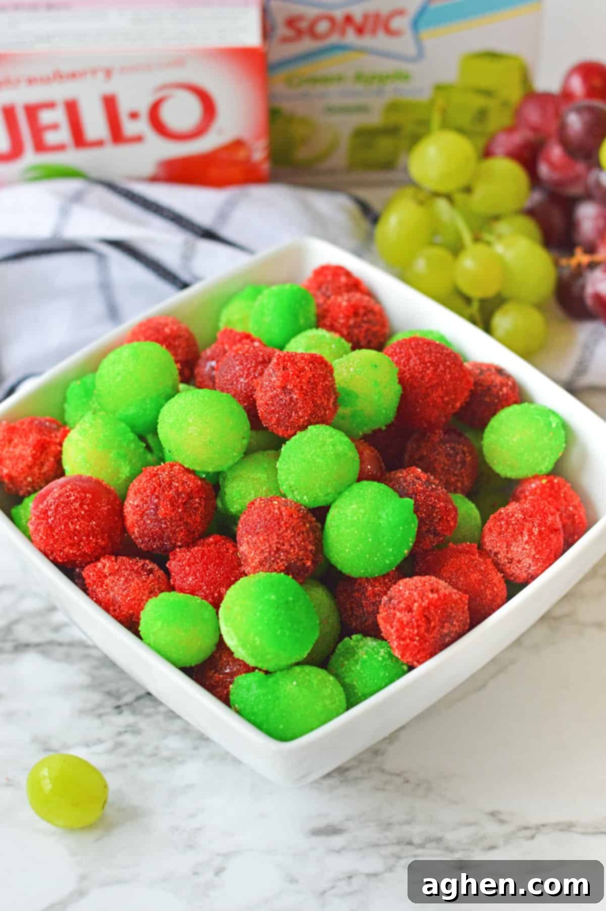 Candied grapes with jello powder in a bowl with fresh grapes and jello mix in the background.