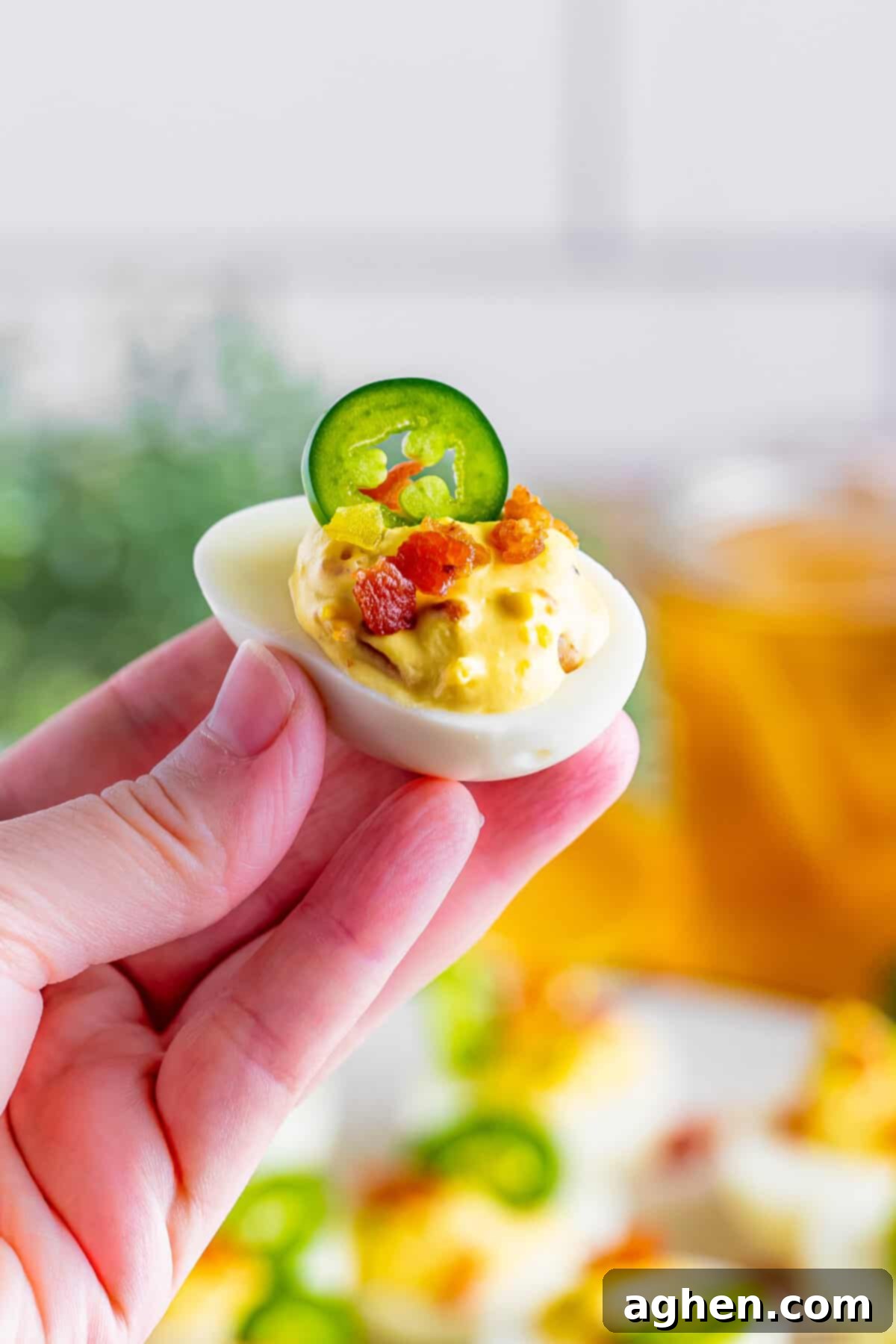 Fiery Deviled Egg Poppers 11 A hand gently holding a single Jalapeno Popper Deviled Egg, showcasing its rich filling and garnishes.