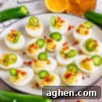 Fiery Deviled Egg Poppers 13 Jalapeno Popper Deviled Eggs with crispy bacon, cream cheese, and fresh jalapenos, arranged neatly on a white serving plate.