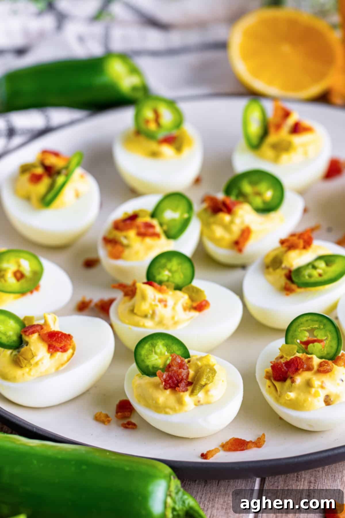 Fiery Deviled Egg Poppers 10 A close-up shot of two Jalapeno Popper Deviled Eggs, richly filled and garnished with crumbled bacon and a single jalapeno slice.