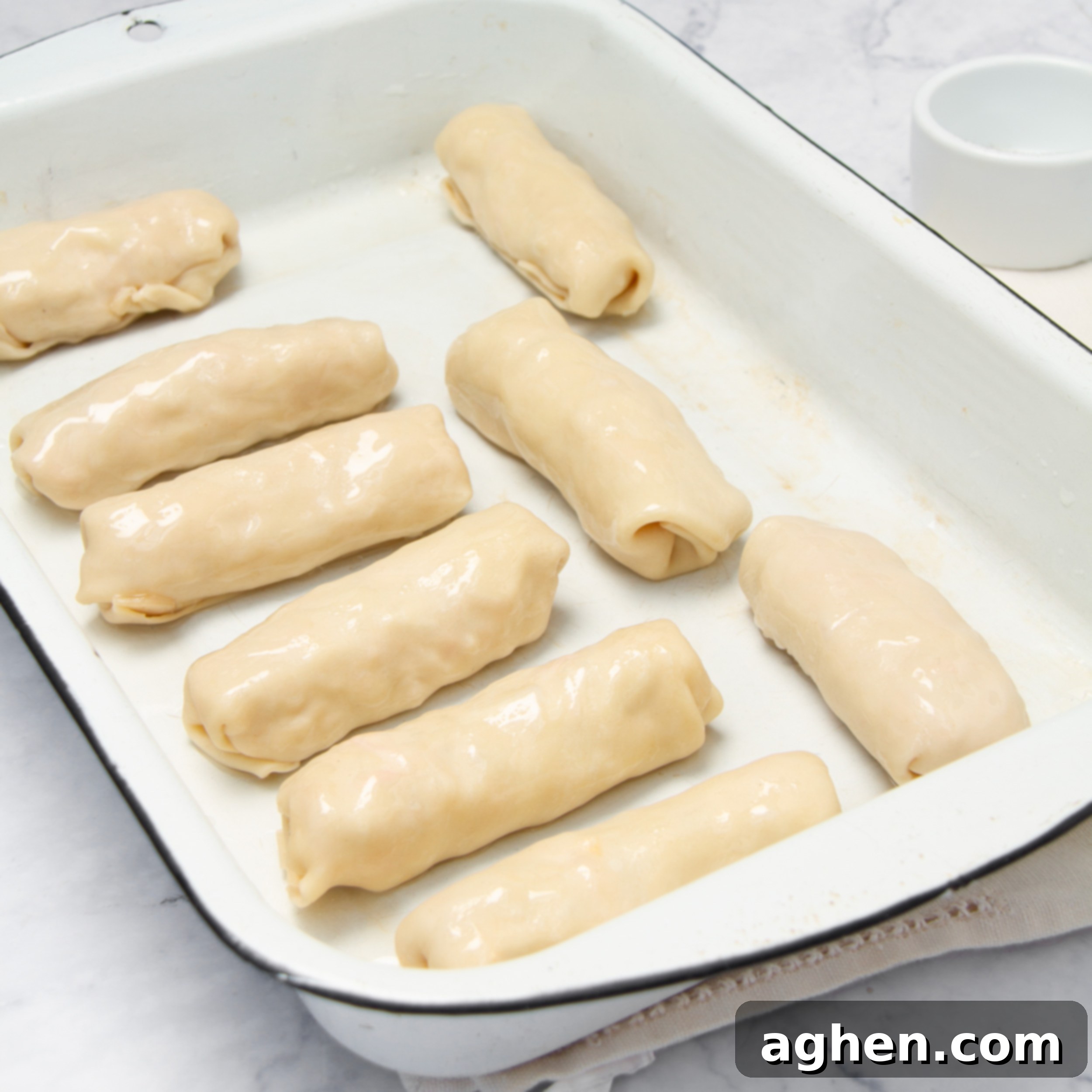Egg rolls rolled up and in an oven dish waiting to be baked. 