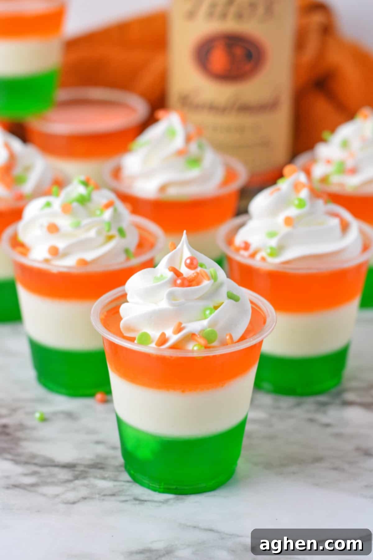 Green, white, and orange layered jello shots with whipped cream and sprinkles, arranged for a festive St. Patrick's Day celebration.