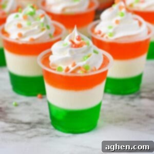Festive St. Patrick's Day jello shots with green, white, and orange layers, whipped cream, and sprinkles.