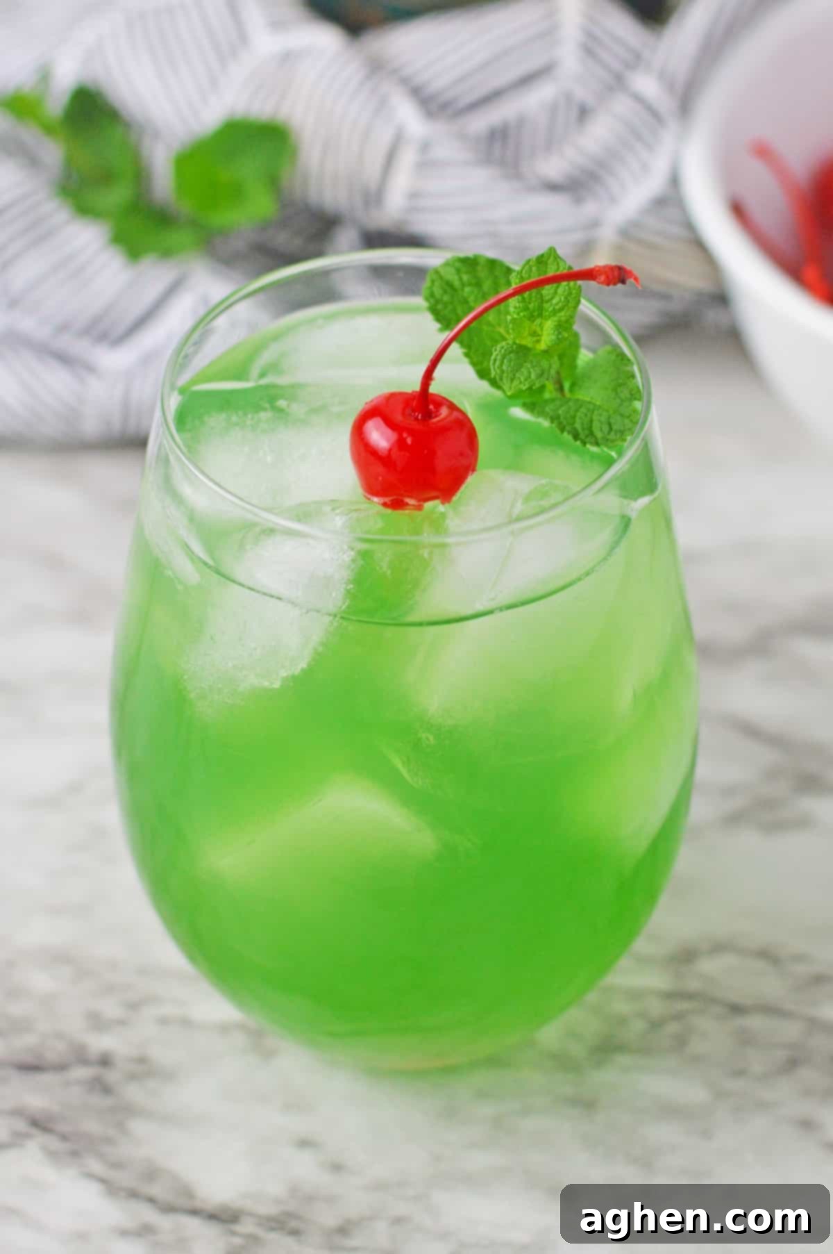 Green cocktail garnished with maraschino cherry and fresh mint.