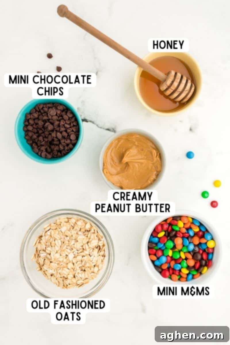Individual bowls displaying the core ingredients for monster energy balls: honey, creamy peanut butter, mini chocolate chips, mini M&M's, and old-fashioned oats.
