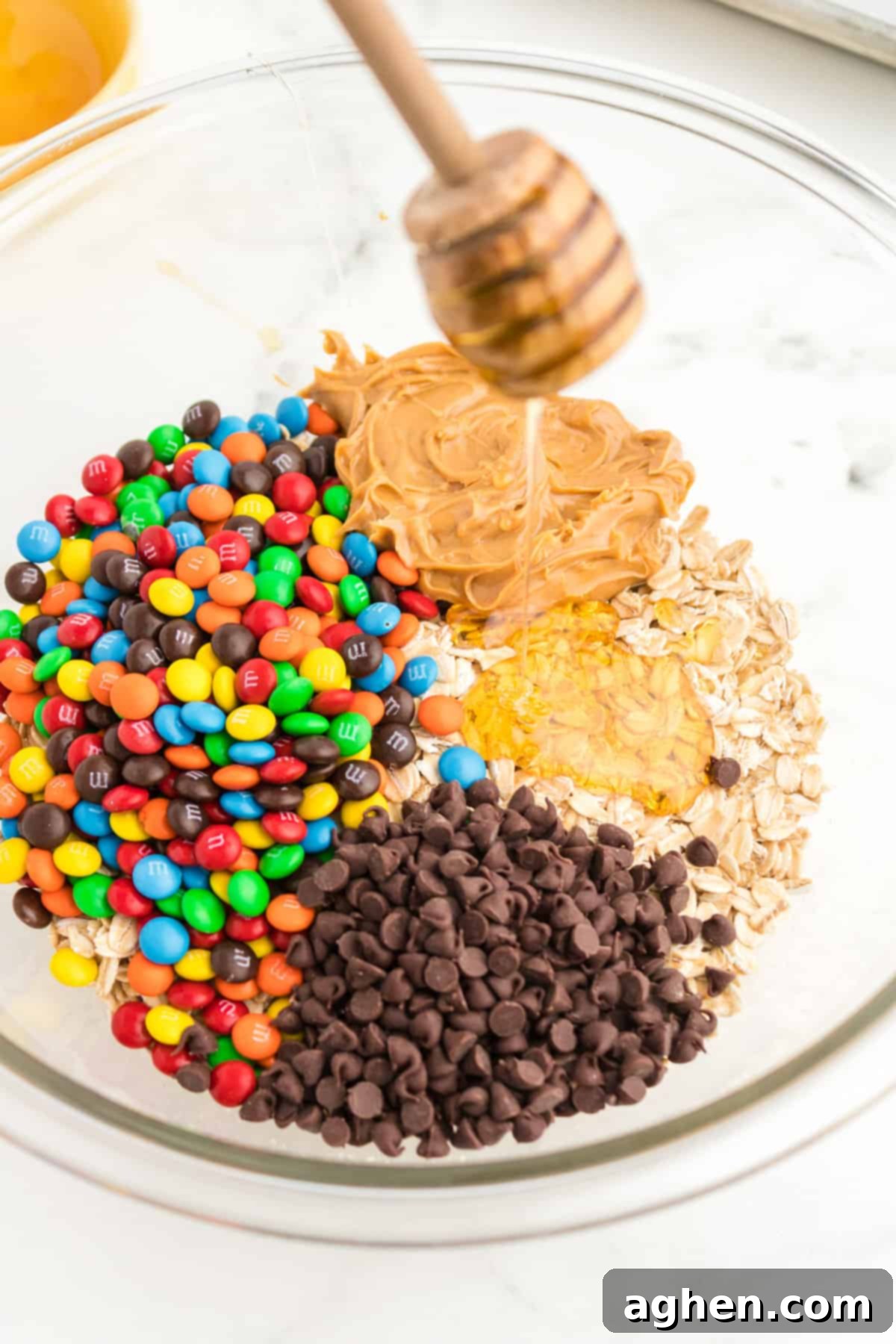 All the dry and wet ingredients for monster energy balls mixed together in a clear glass mixing bowl, ready to be formed.