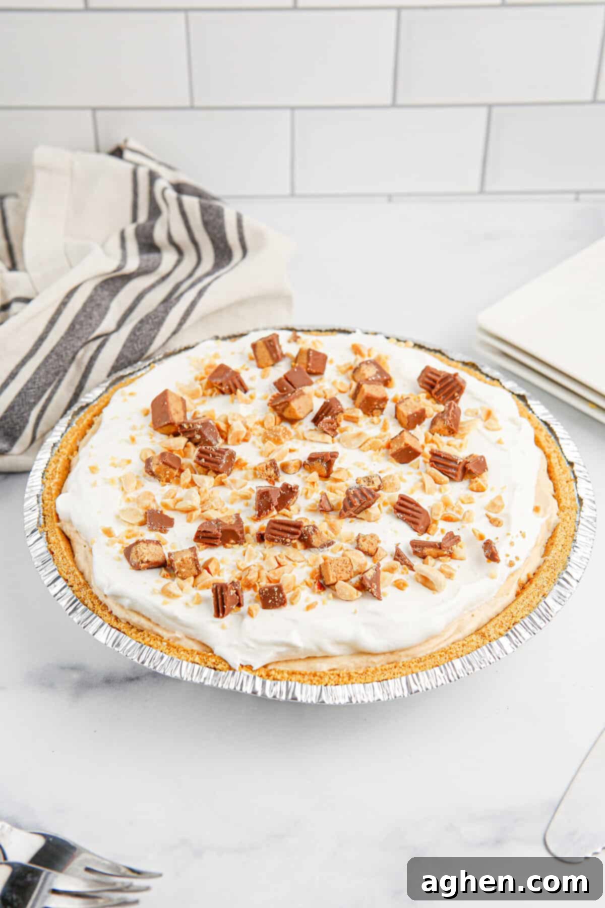 No bake peanut butter pie topped with whipped topping, Reese's peanut butter cups, and peanuts, ready to be served.