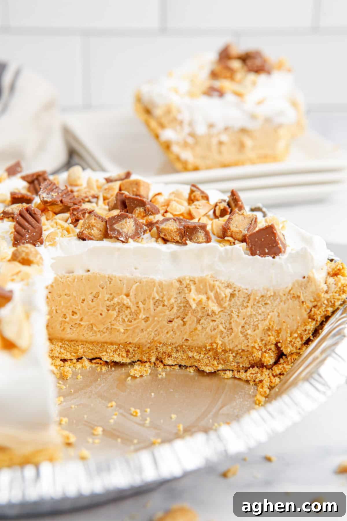 Side-view of peanut butter pie in foil tin with slice removed, showing distinct layers of creamy peanut butter pie and whipped topping.