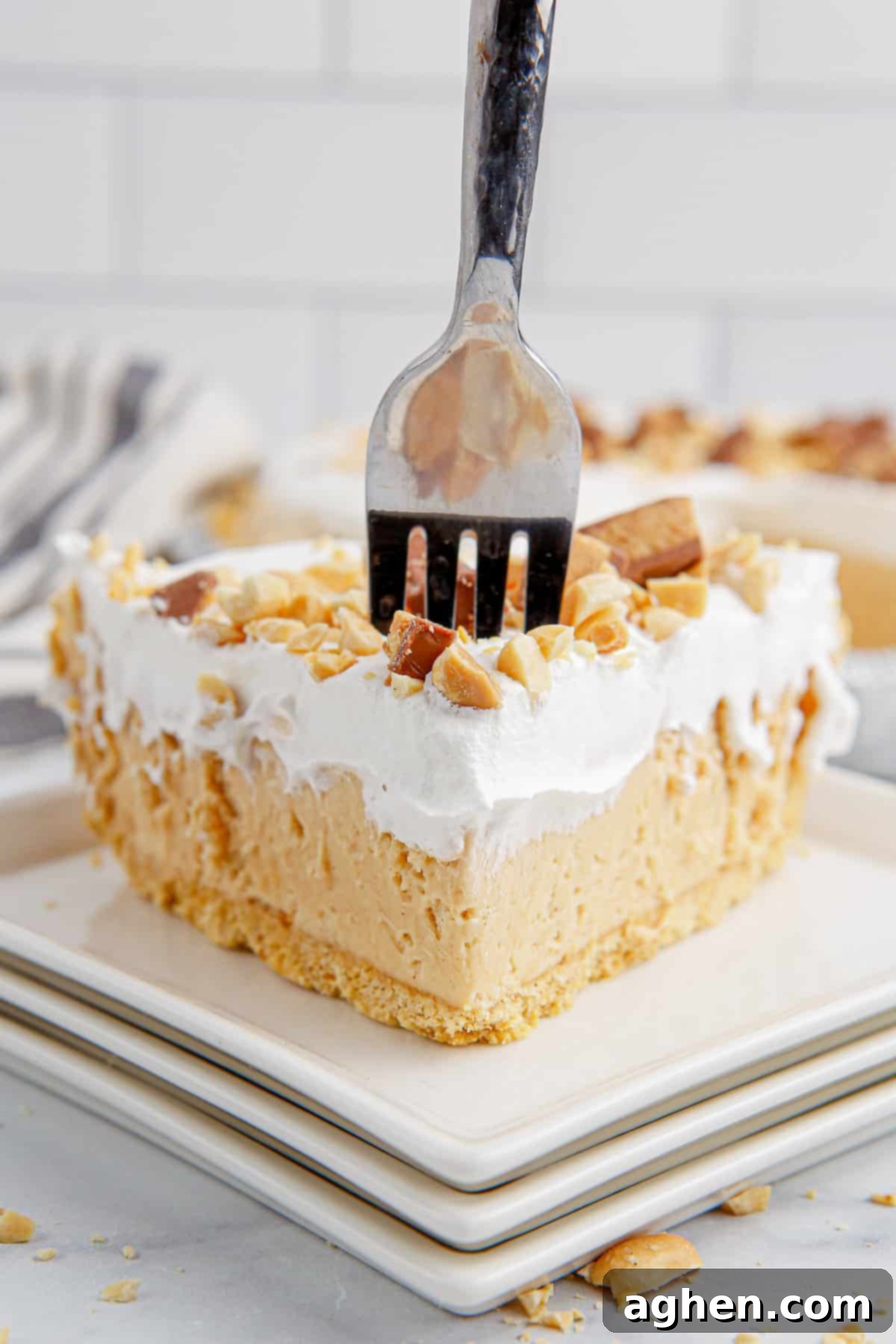 Fork going in to a slice of peanut butter pie topped with cool whip and Reese's, showing its creamy texture.