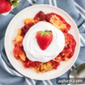 Strawberry dump cake on a white plate topped with cool whip and a fresh strawberry.