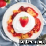 Strawberry dump cake on a white plate topped with cool whip and a fresh strawberry.