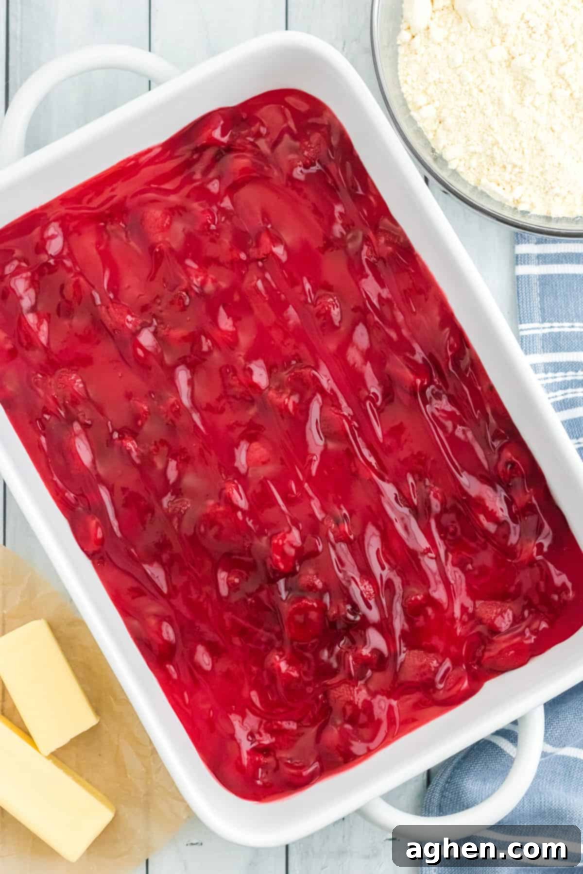 Vibrant red strawberry pie filling spread in an even, luscious layer across the bottom of a white 9 x 13 baking dish, ready for the next step.