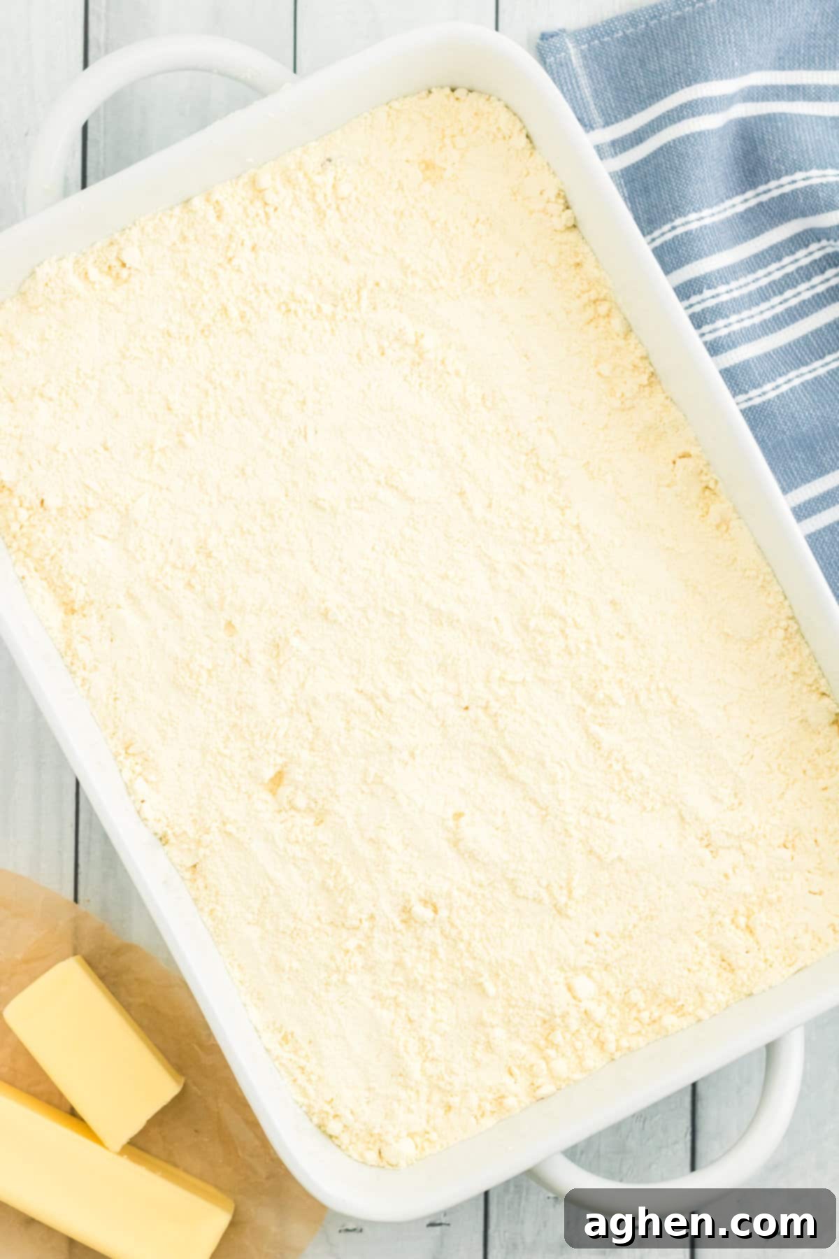 Dry yellow cake mix lightly and evenly covering the strawberry pie filling in the baking dish, creating a blanket over the fruit layer.
