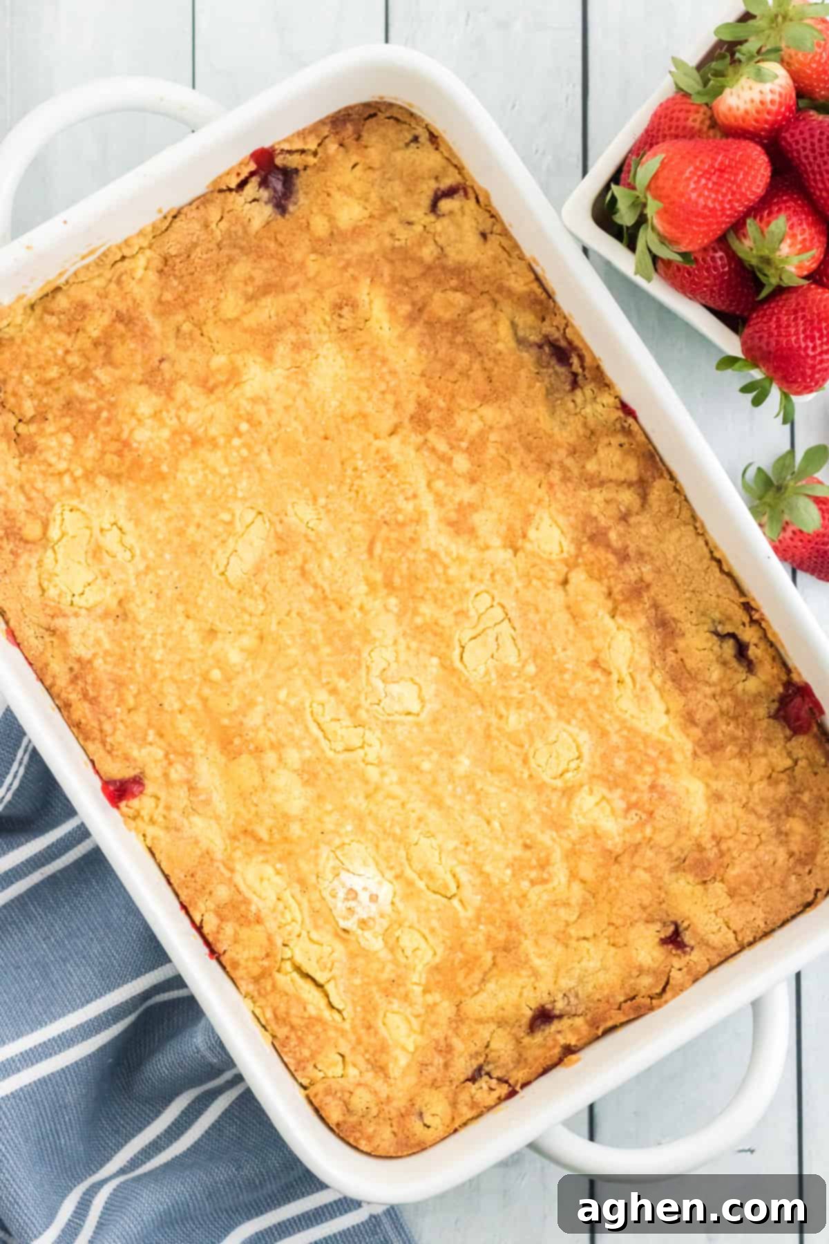 A perfectly baked Strawberry Dump Cake, golden brown and bubbly around the edges, just removed from the oven in a white baking dish, ready to be served.