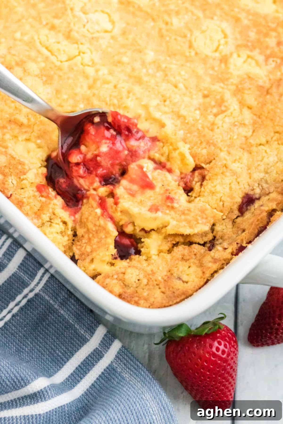 A large spoon breaking through the golden, crisp surface of a freshly baked dump cake, revealing the warm, gooey strawberry pie filling bubbling beneath, showcasing the delicious texture.