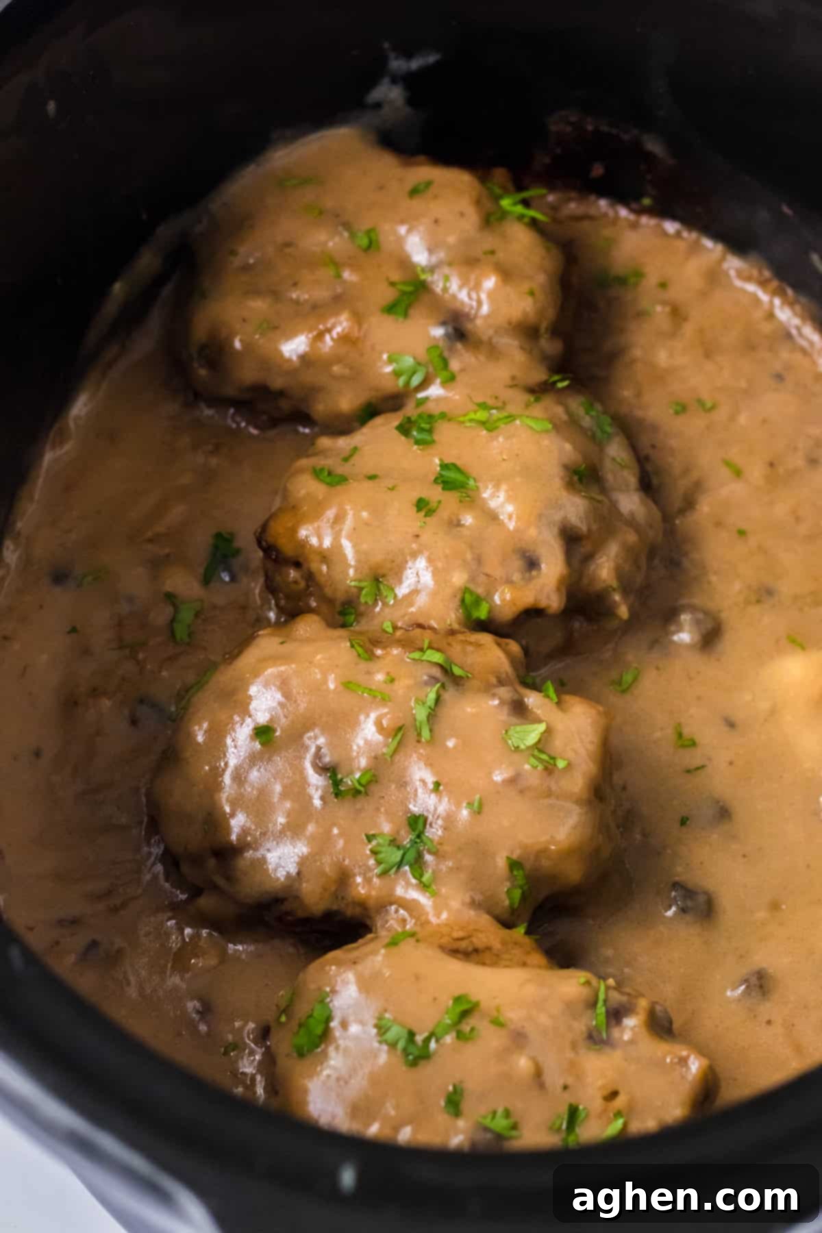 Easy Slow Cooker Salisbury Steaks 3 Slow cooker Salisbury steaks smothered with rich brown gravy and garnished with fresh parsley in a crockpot.