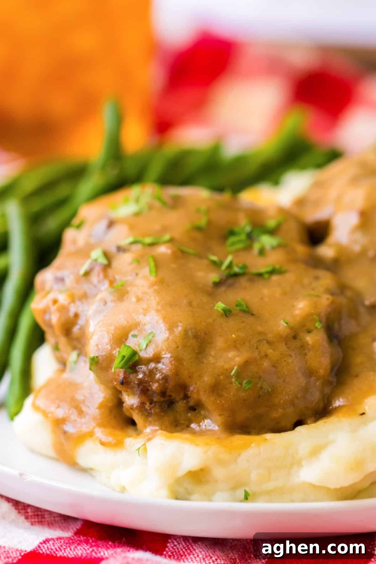 Easy Slow Cooker Salisbury Steaks 10 Side view of a thick hamburger steak patty sitting on a bed of mashed potatoes and covered with luscious brown gravy.