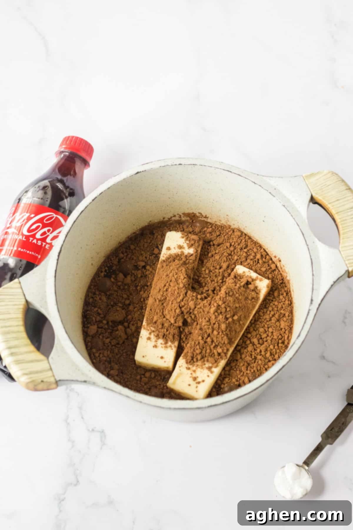 Decadent Double Chocolate Coca Cola Cake 5 A saucepan on a stove with cocoa powder and two sticks of butter melting into Coca-Cola, ready to be whisked and brought to a boil for the cake batter.