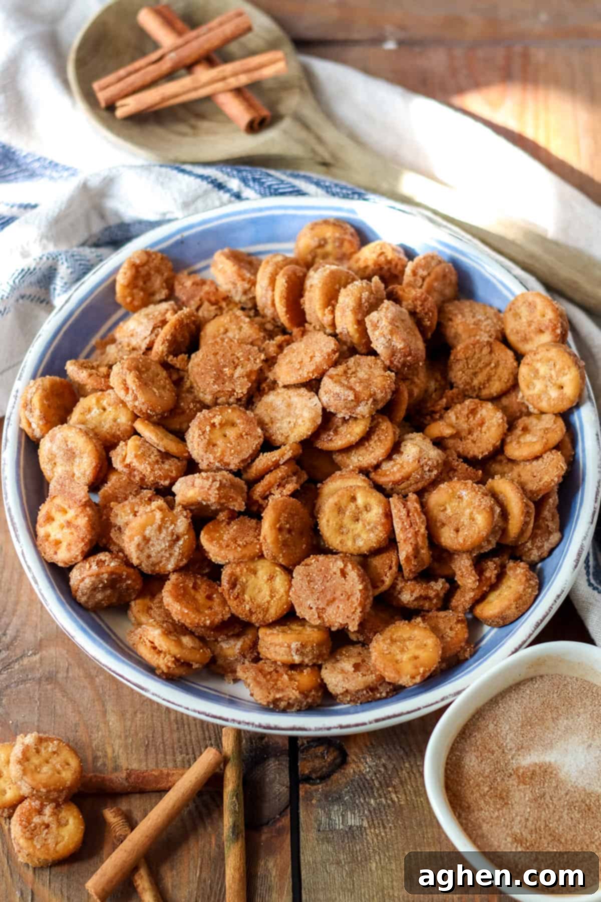 Cinnamon Ritz Churro Bites 2 Cinnamon sugar Ritz Churro Bites in a large serving bowl on a wooden table with a small bowl of cinnamon sugar and cinnamon sticks around it.
