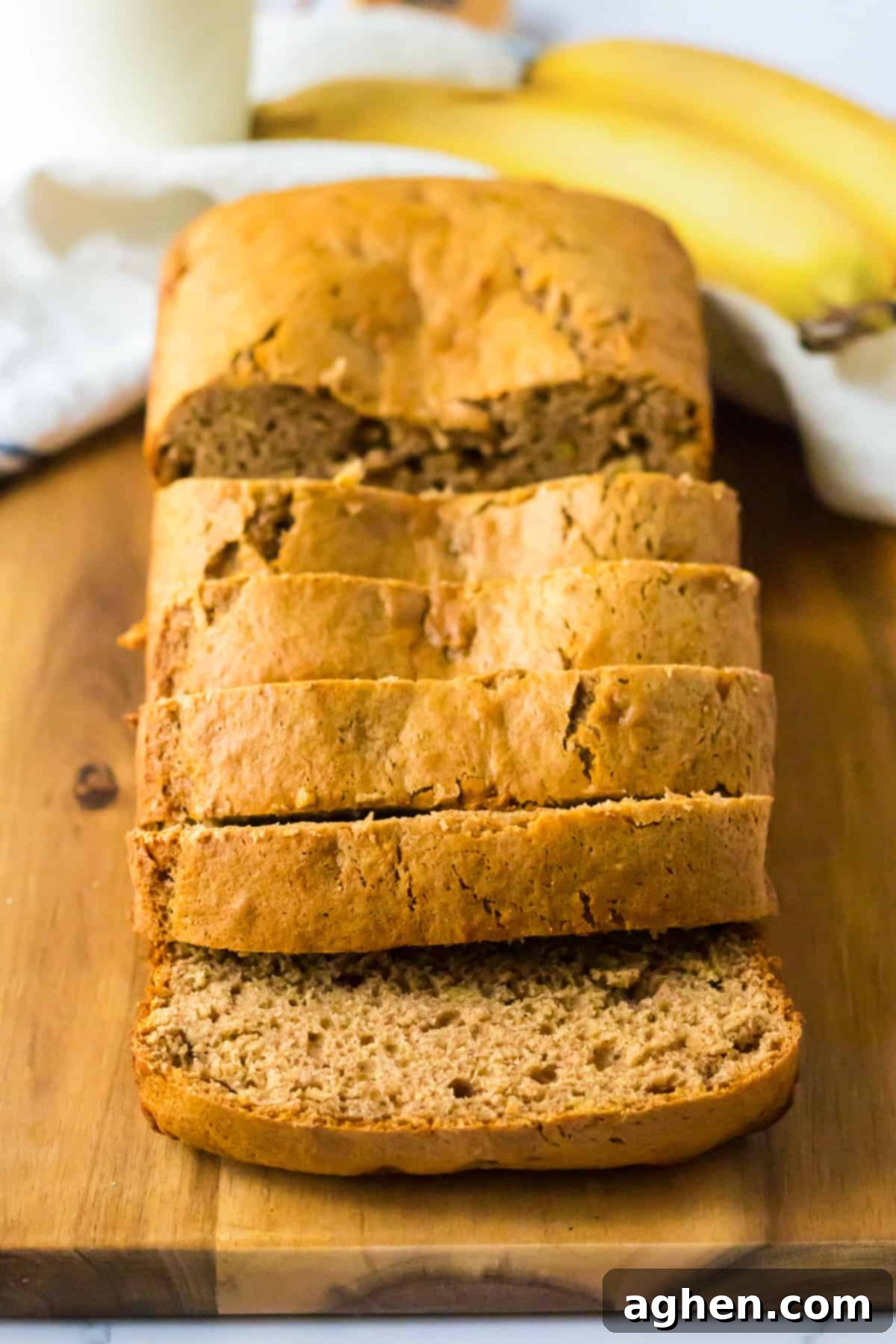 Sliced loaf of banana bread on cutting board with fresh bananas behind it.