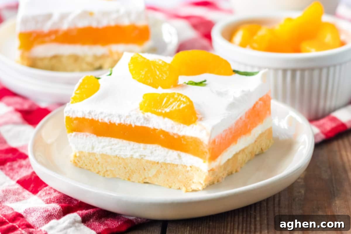 Velvet Orange Dream 9 A visually appealing shot of the Orange Creamsicle Lush, featuring its distinct layers of creamy vanilla pudding, orange jello, sweetened cream cheese, and cool whip atop a sweet cookie crust. The dessert is garnished with vibrant mandarin orange pieces, highlighting its refreshing no-bake nature.