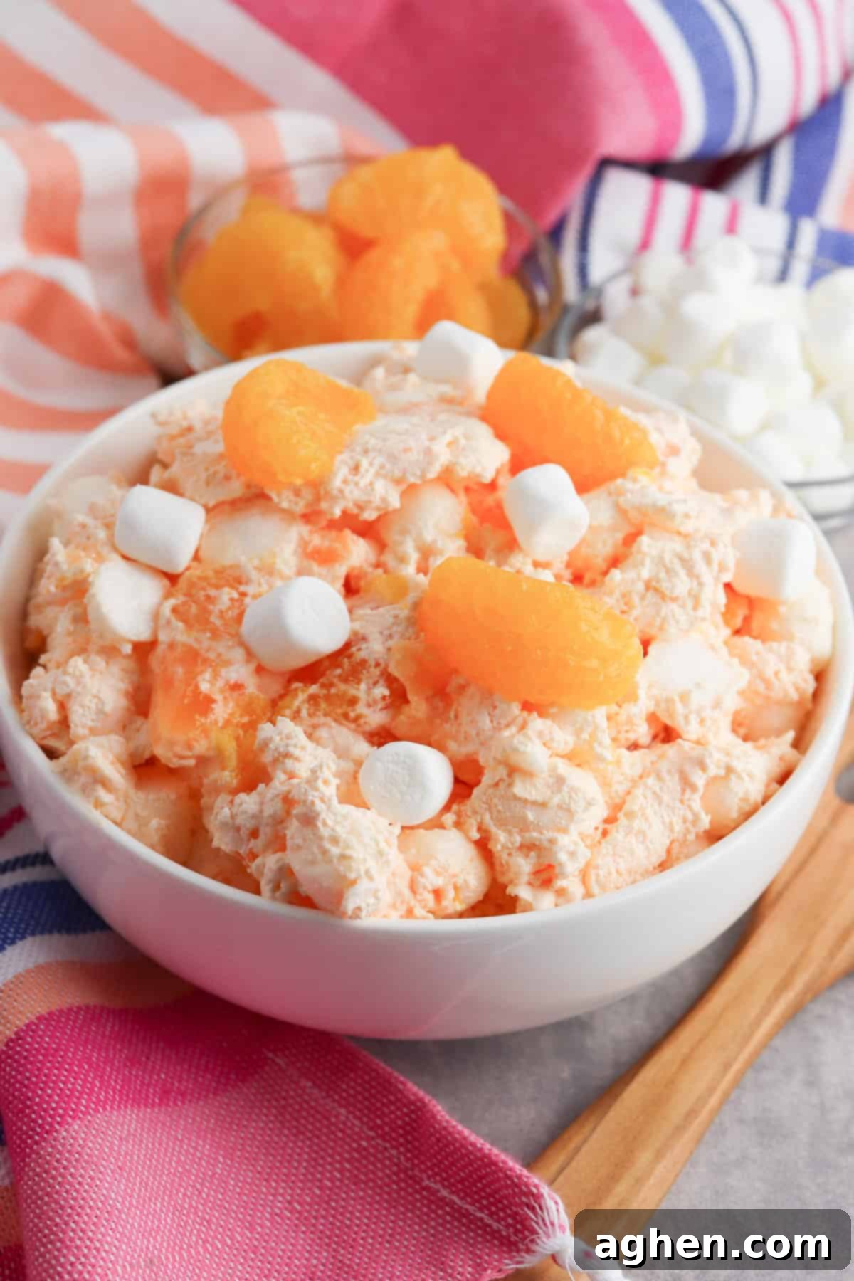 Vibrant orange fluff salad featuring mini marshmallows, tender mandarin oranges, and set orange jello, ready to be served.