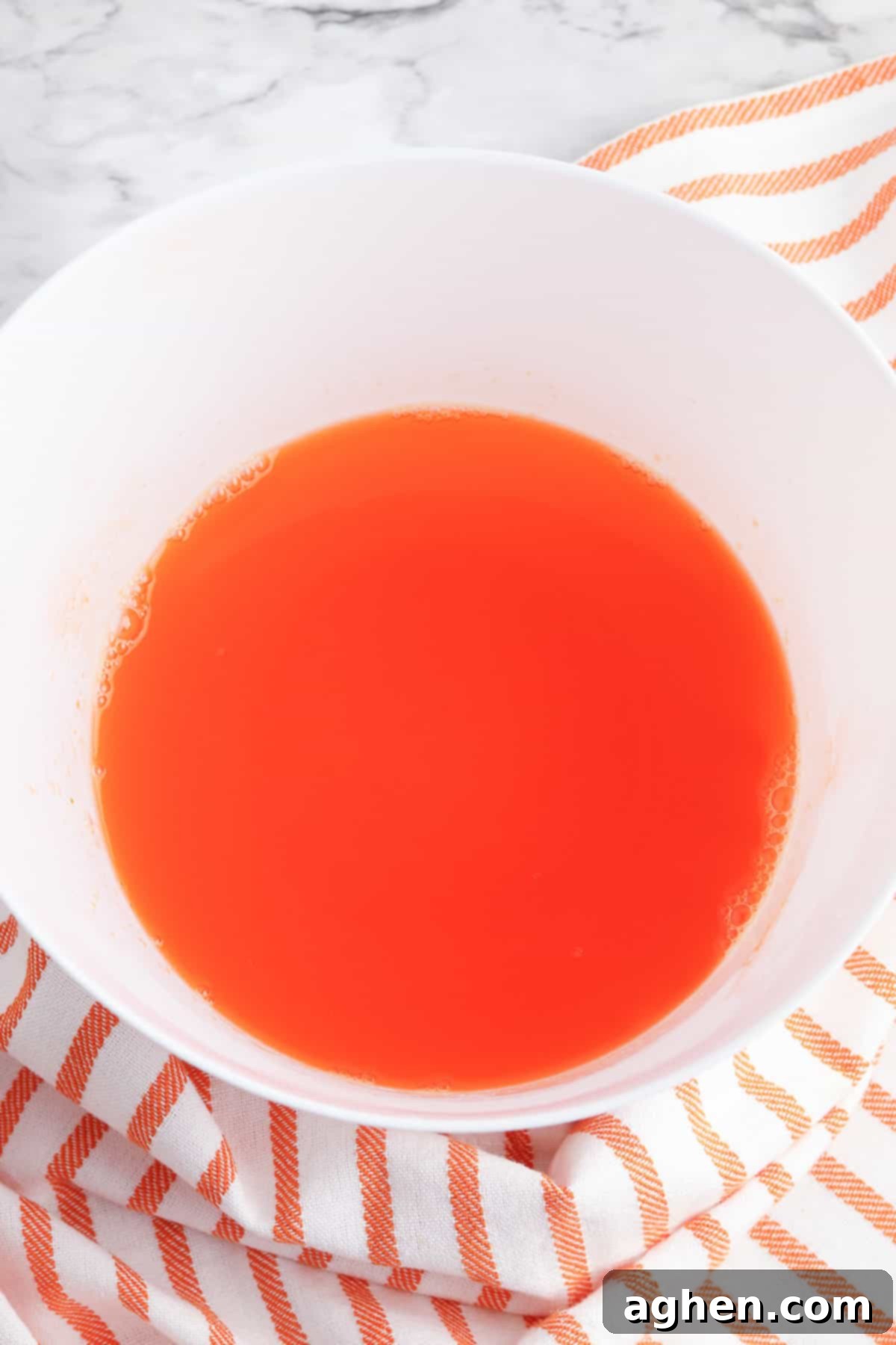 Orange jello mixture in a clear mixing bowl, ready for chilling.