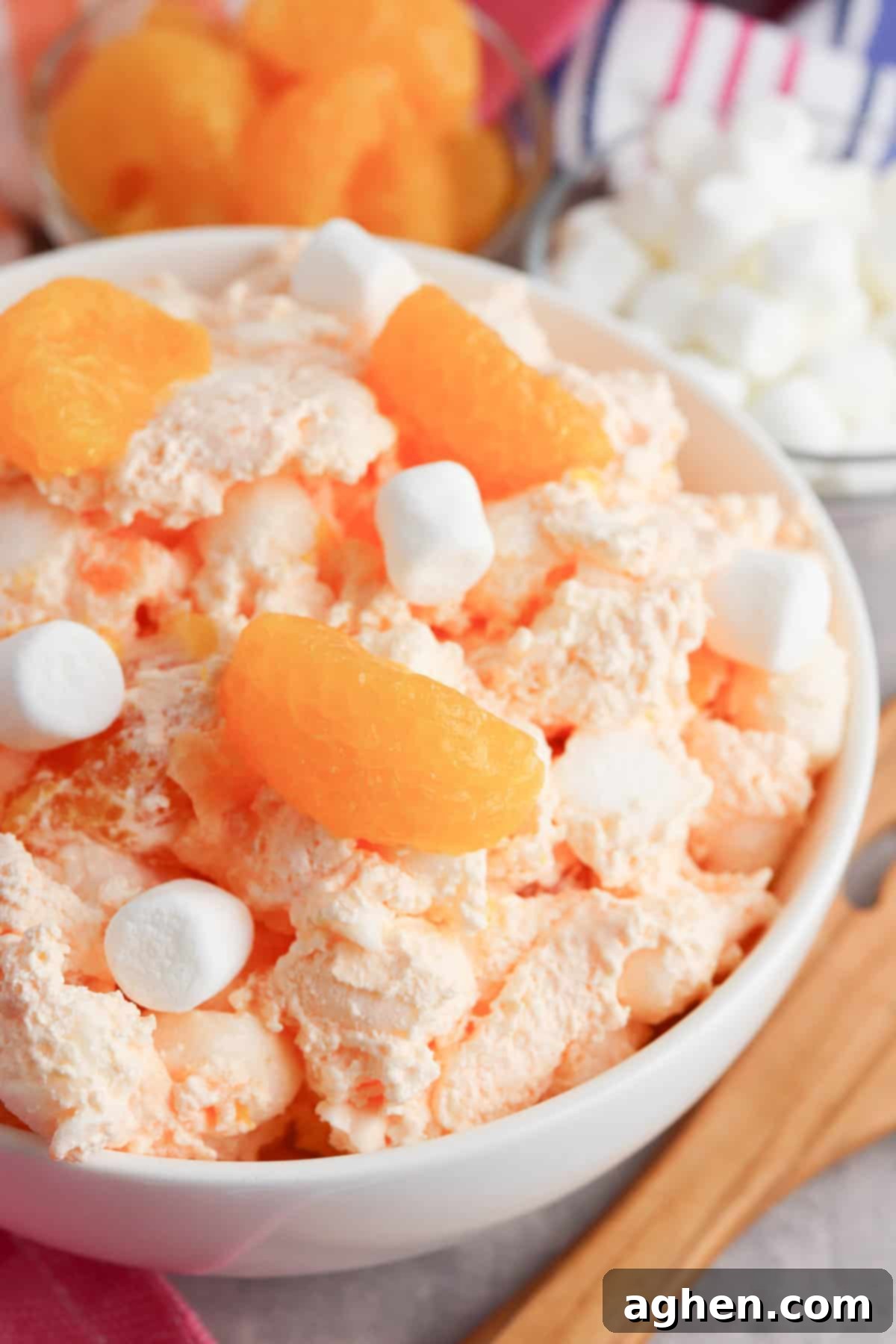 A bowl of creamy orange creamsicle salad, served with a wooden serving spoon, showcases its fluffy texture and vibrant color.