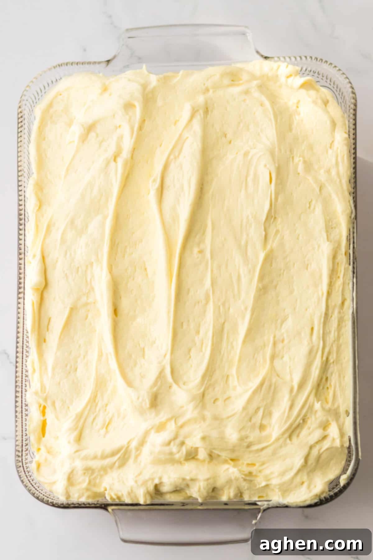 Banana Cream Dream Poke Cake 8 A yellow poke cake is shown completely covered with a thick, even layer of the creamy banana pudding and cream cheese mixture, having been gently pressed into all the holes.