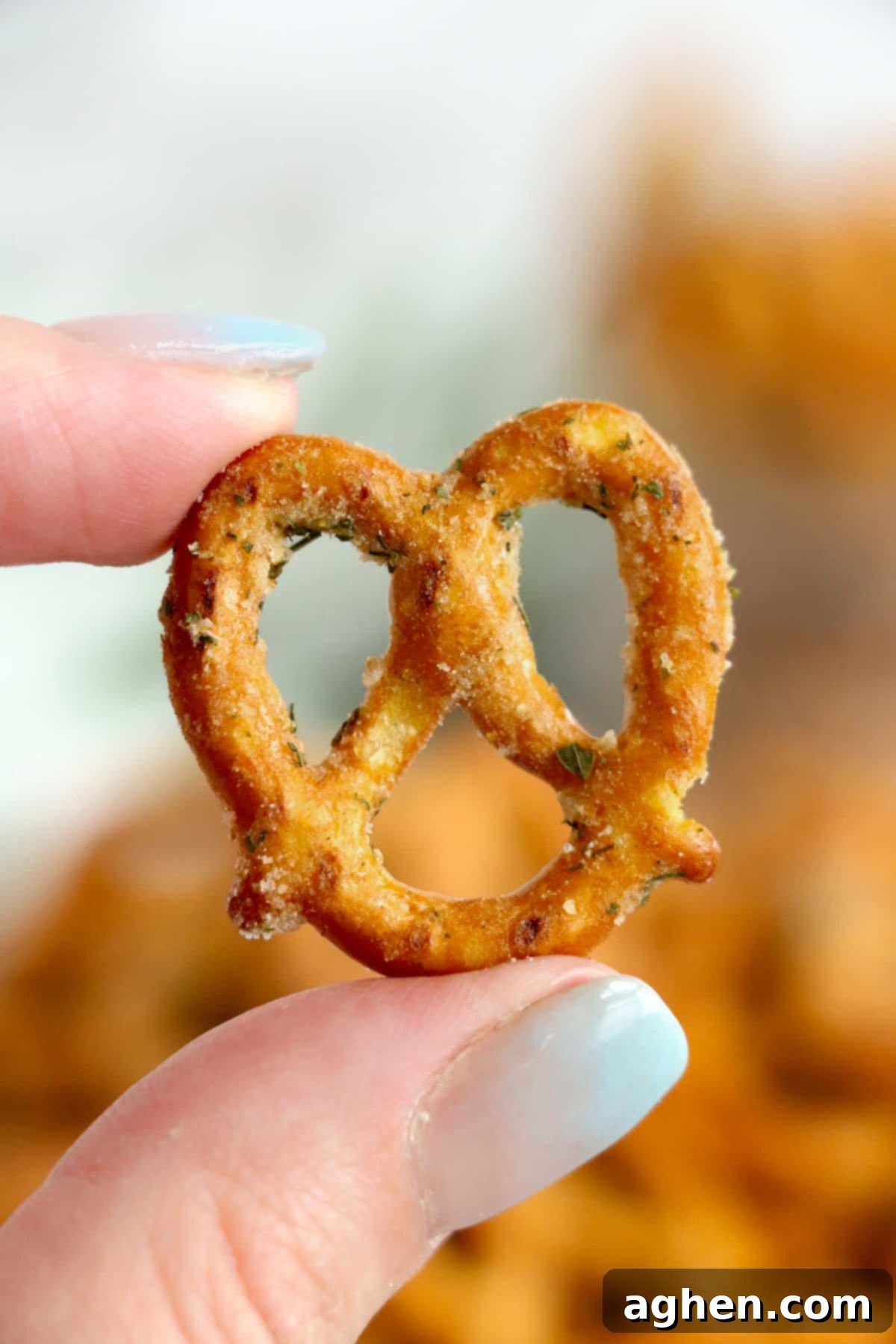 A hand gently holding a homemade seasoned pretzel, showcasing its golden hue and delicious seasoning.