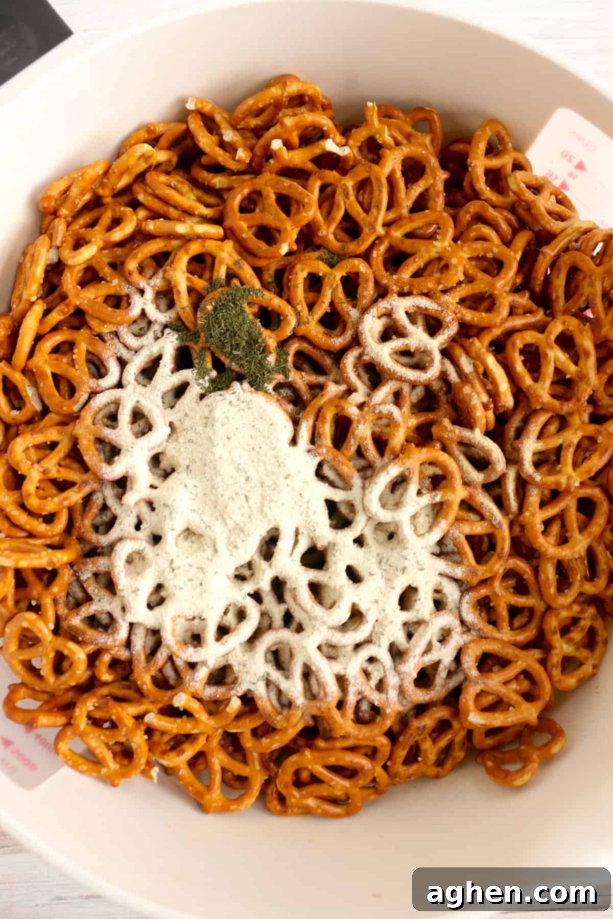 Ranch mix and other seasonings, including garlic powder, onion powder, and dill weed, lightly sprinkled over pretzel twists in a large mixing bowl.